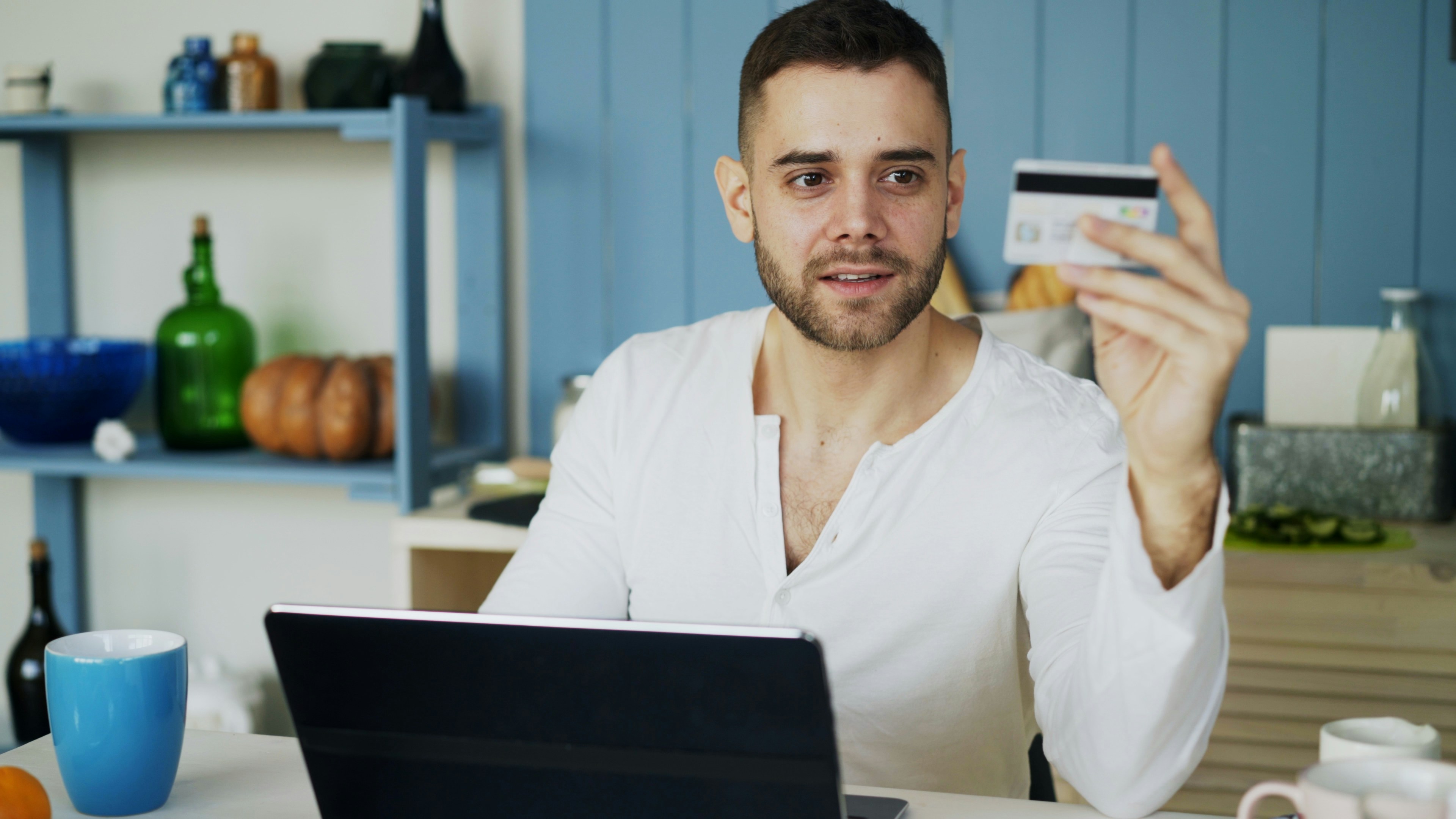 Young man having online shopping using credit card and laptop computer while have breakfast in the kitchen at home in the morning